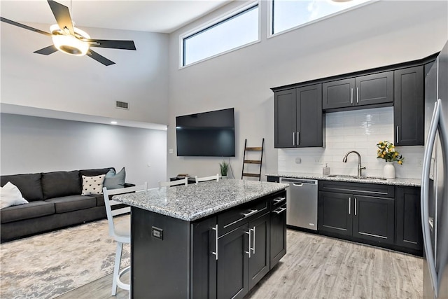 kitchen featuring appliances with stainless steel finishes, open floor plan, a sink, a kitchen island, and dark cabinets