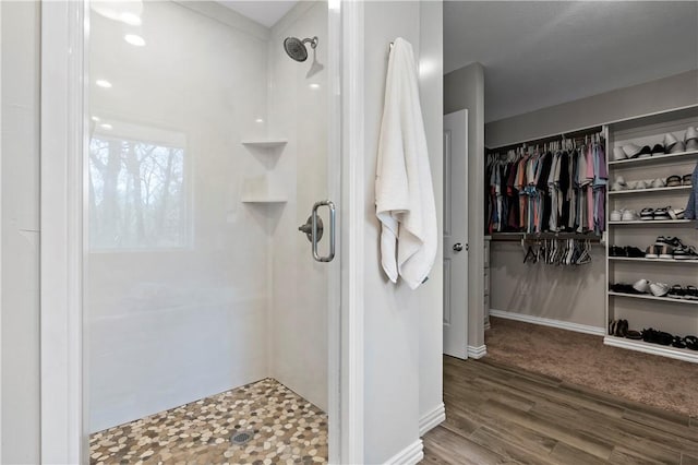 bathroom with a walk in closet, wood finished floors, and a walk in shower