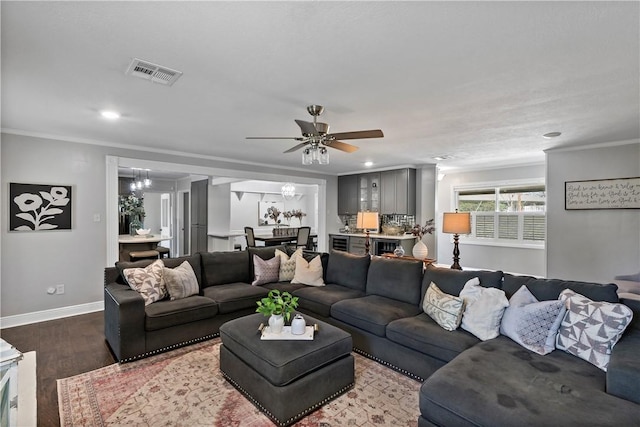 living area featuring ceiling fan with notable chandelier, wood finished floors, visible vents, and ornamental molding