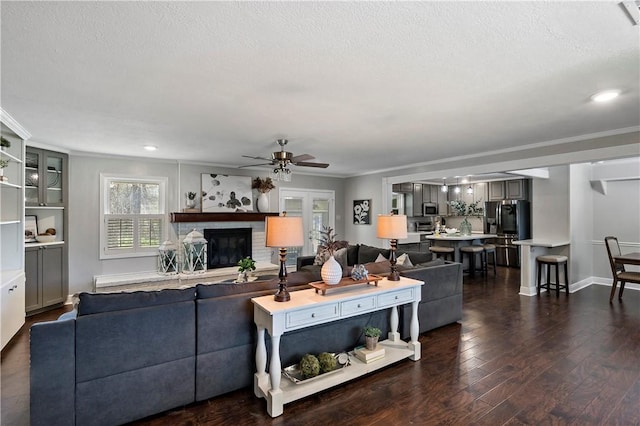 living area featuring a glass covered fireplace, dark wood-style floors, crown molding, baseboards, and ceiling fan