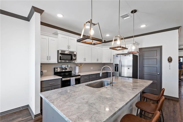 kitchen featuring white cabinets, a center island with sink, sink, hanging light fixtures, and appliances with stainless steel finishes