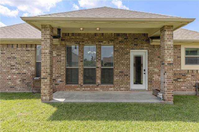 8305 Raintree Dr, College Station, TX 77845 - doorway to property featuring a shingled roof, brick siding, a lawn, and a patio