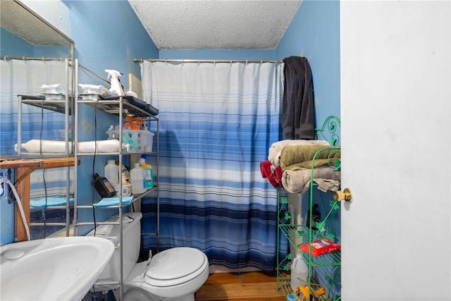 full bathroom featuring a shower with shower curtain, a textured ceiling, toilet, a sink, and wood finished floors