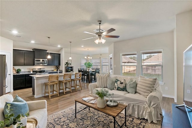 living room with ceiling fan with notable chandelier and light hardwood / wood-style flooring