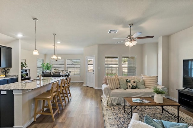 living room featuring wood-type flooring, ceiling fan with notable chandelier, a textured ceiling, and sink