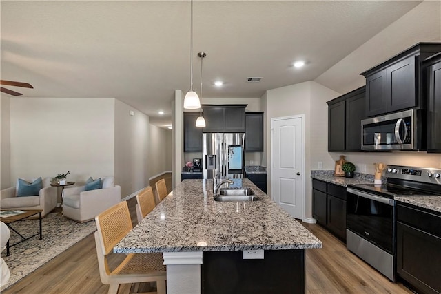 kitchen featuring appliances with stainless steel finishes, light wood-type flooring, a kitchen breakfast bar, a center island with sink, and hanging light fixtures