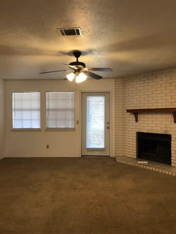 unfurnished living room featuring visible vents, a ceiling fan, a brick fireplace, carpet flooring, and a textured ceiling