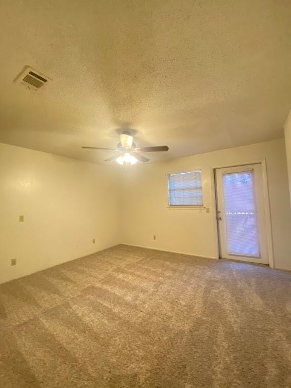 carpeted spare room featuring a textured ceiling, visible vents, and a ceiling fan