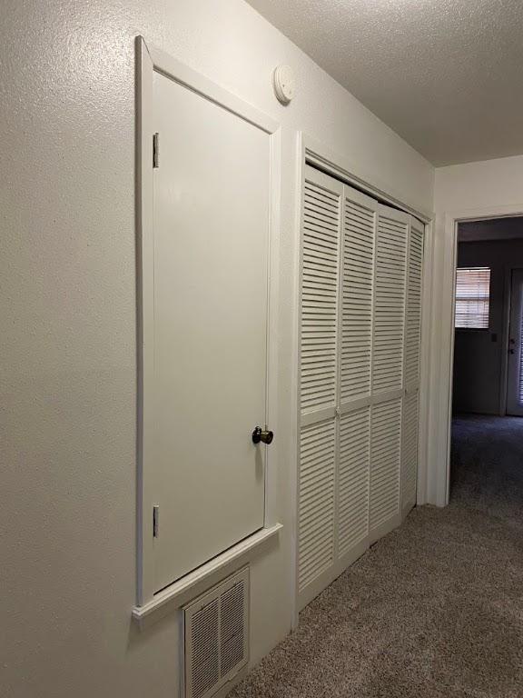 corridor with a textured ceiling, carpet floors, a textured wall, and visible vents