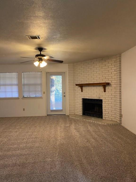 unfurnished living room with a brick fireplace, a textured ceiling, visible vents, and carpet flooring