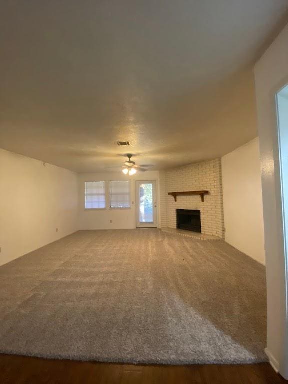 unfurnished living room featuring a ceiling fan, dark carpet, visible vents, and a fireplace