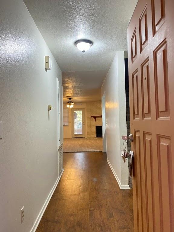 hall featuring a textured ceiling, baseboards, and dark wood-type flooring