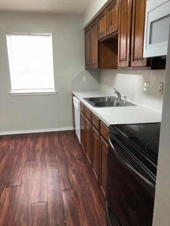 kitchen featuring dark wood finished floors, light countertops, a sink, white appliances, and baseboards