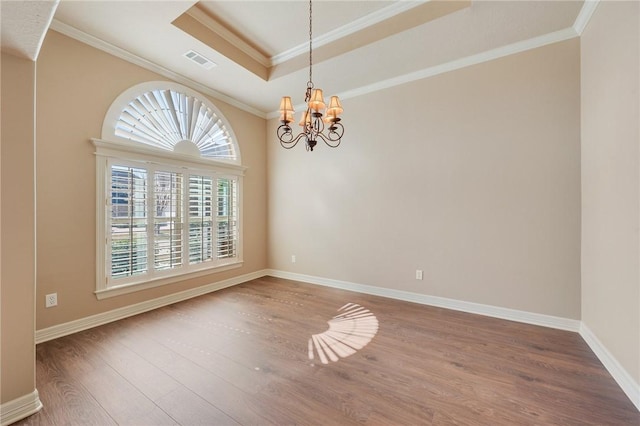 spare room with a tray ceiling, crown molding, wood finished floors, and visible vents