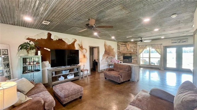 living room with concrete floors, a stone fireplace, and ceiling fan