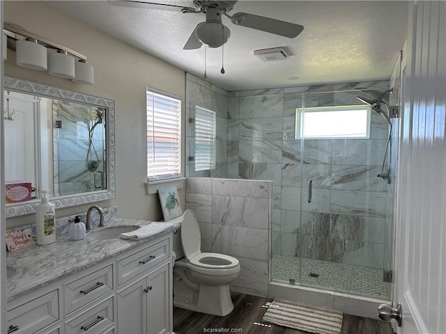 full bathroom featuring ceiling fan, a shower stall, toilet, wood finished floors, and vanity