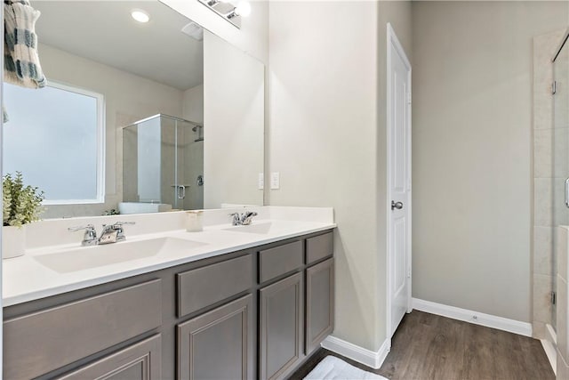 full bathroom featuring double vanity, a sink, a shower stall, wood finished floors, and baseboards