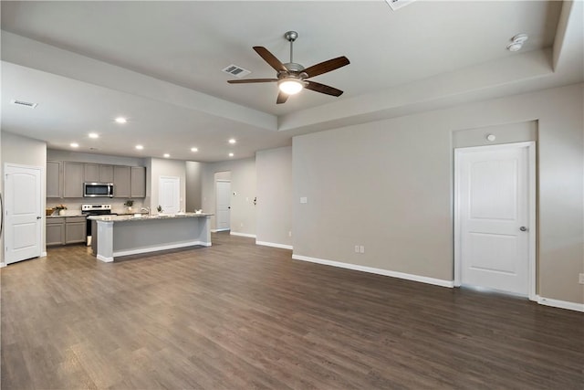 unfurnished living room featuring recessed lighting, visible vents, baseboards, a tray ceiling, and dark wood finished floors