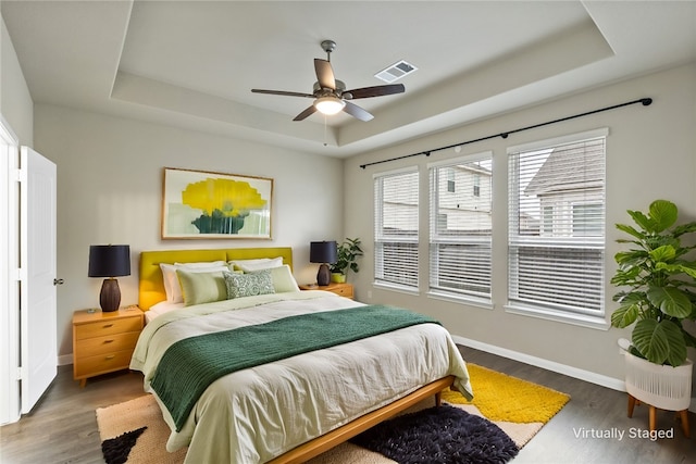 bedroom with dark wood-style floors, visible vents, a tray ceiling, and baseboards