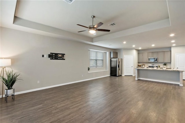 living area with visible vents, a tray ceiling, and baseboards