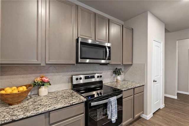 kitchen with appliances with stainless steel finishes, dark wood-type flooring, light stone counters, and tasteful backsplash