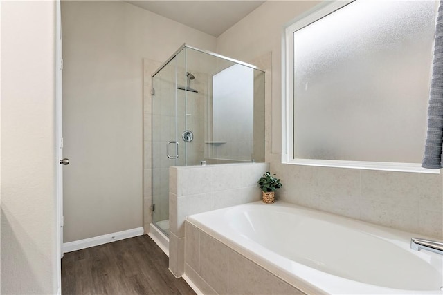 full bath featuring a shower stall, baseboards, a bath, and wood finished floors