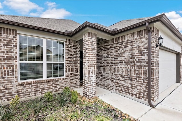 property entrance featuring driveway, brick siding, and an attached garage