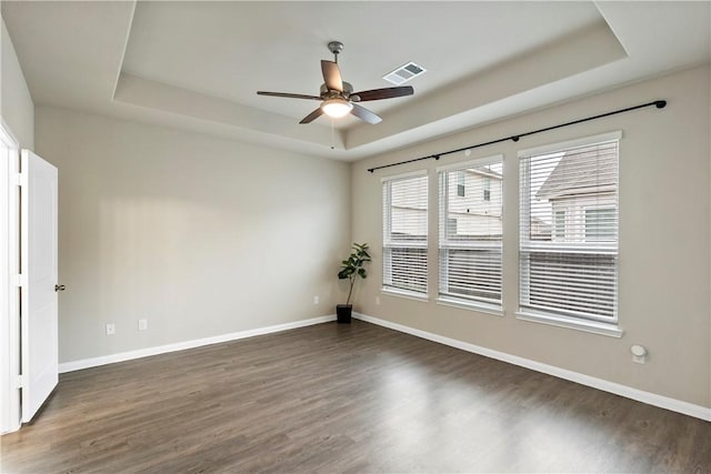 empty room featuring a tray ceiling, dark wood-style flooring, visible vents, and baseboards