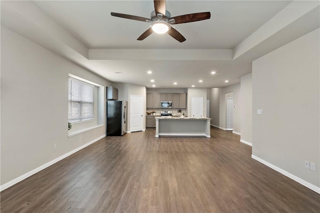 unfurnished living room featuring ceiling fan, recessed lighting, baseboards, dark wood-style floors, and a tray ceiling