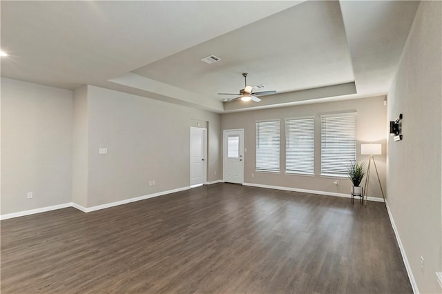 interior space with baseboards, visible vents, a ceiling fan, dark wood-type flooring, and a tray ceiling