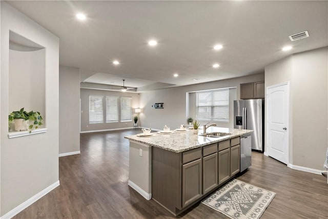 kitchen with a center island with sink, stainless steel appliances, visible vents, a sink, and light stone countertops