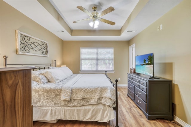 bedroom with a tray ceiling, ceiling fan, and light hardwood / wood-style flooring