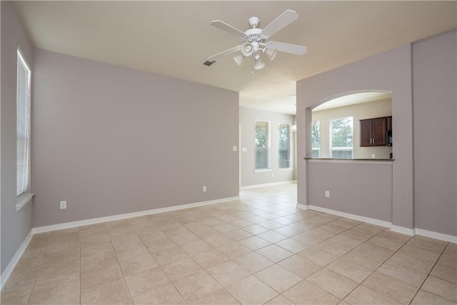 empty room with light tile patterned floors, arched walkways, visible vents, baseboards, and a ceiling fan