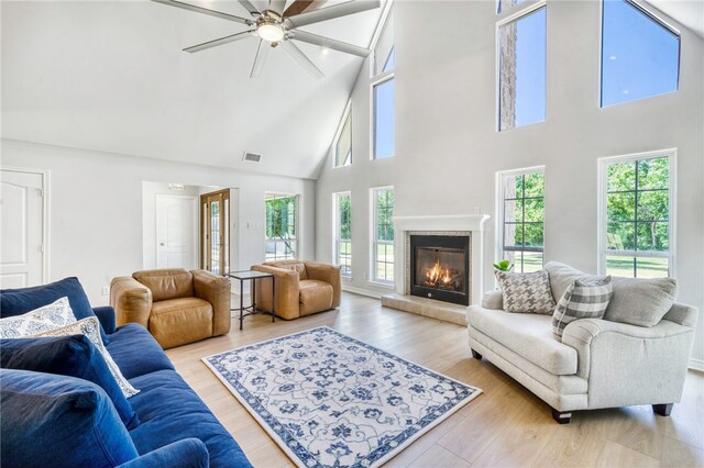 living area with light wood-style floors, high vaulted ceiling, a glass covered fireplace, a ceiling fan, and visible vents