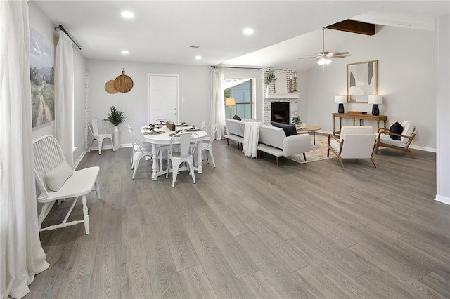 dining area with light wood-type flooring, lofted ceiling with beams, a stone fireplace, and ceiling fan