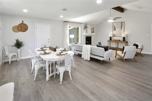 dining room featuring a fireplace, vaulted ceiling with beams, light hardwood / wood-style flooring, and ceiling fan