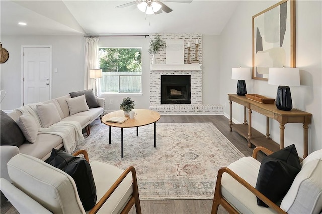 living room featuring ceiling fan, a large fireplace, dark wood-type flooring, and vaulted ceiling