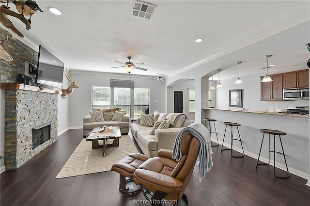 living room featuring dark hardwood / wood-style flooring, a stone fireplace, ceiling fan, and crown molding