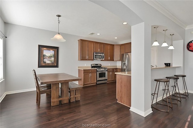 kitchen featuring dark hardwood / wood-style flooring, ornamental molding, hanging light fixtures, and appliances with stainless steel finishes