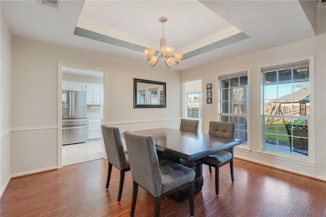 dining area featuring a notable chandelier, light hardwood / wood-style floors, and a tray ceiling