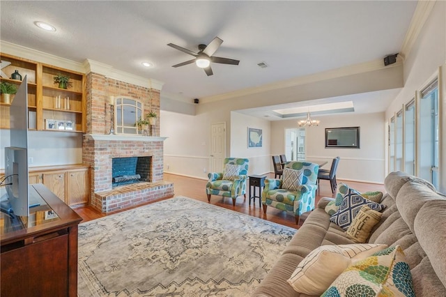 living room featuring a fireplace, ornamental molding, ceiling fan with notable chandelier, and hardwood / wood-style flooring