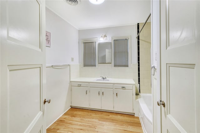 bathroom with hardwood / wood-style floors, vanity, tiled shower / bath, and ornamental molding