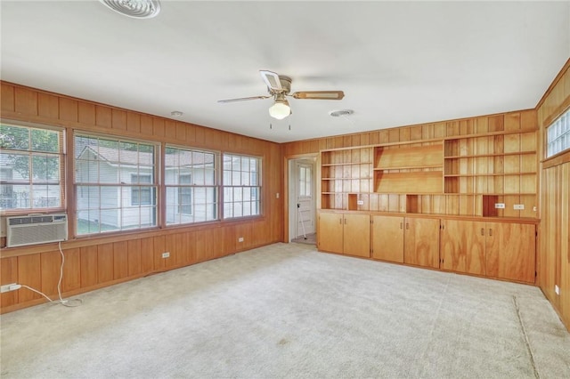 unfurnished living room featuring wooden walls, cooling unit, light carpet, and ceiling fan