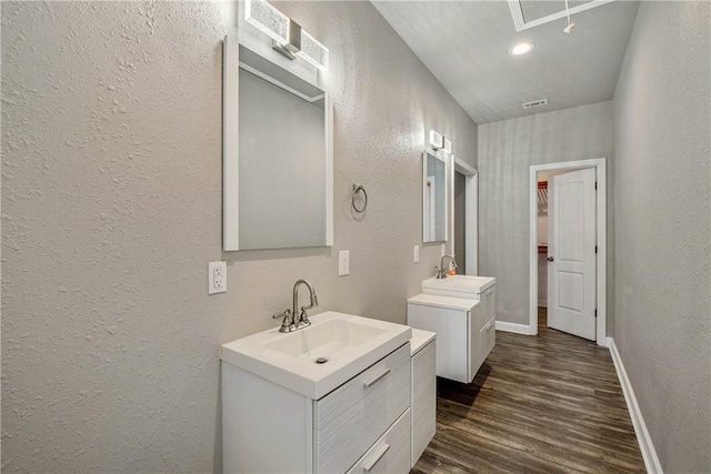 bathroom with two vanities, visible vents, wood finished floors, a textured wall, and baseboards