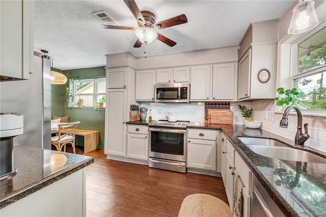 kitchen with appliances with stainless steel finishes, a sink, dark wood finished floors, a ceiling fan, and backsplash