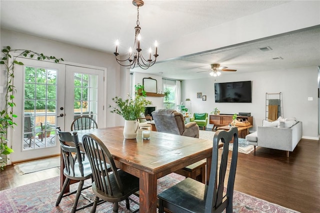 dining space with visible vents, a fireplace, wood finished floors, baseboards, and ceiling fan with notable chandelier