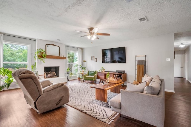 living room featuring ceiling fan, a brick fireplace, a textured ceiling, wood finished floors, and visible vents