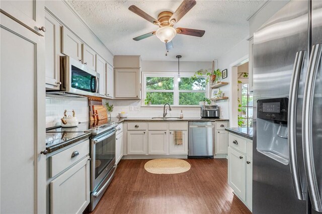kitchen featuring dark wood-style floors, a textured ceiling, tasteful backsplash, a sink, and appliances with stainless steel finishes