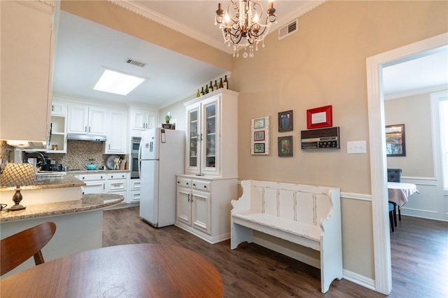 kitchen featuring pendant lighting, dark wood-type flooring, white cabinets, white refrigerator, and light stone counters