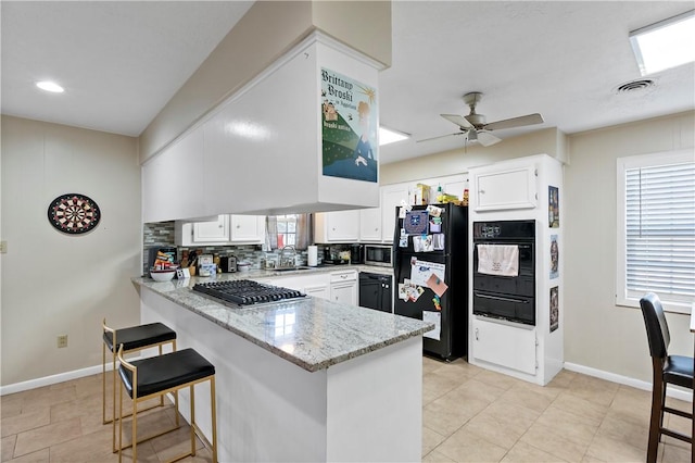 kitchen with tasteful backsplash, a peninsula, black appliances, a warming drawer, and a sink